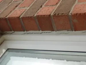 Caulking cracked around a window, beside brick wall.